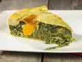 Una fetta di torta di bietole e ricotta senza sfoglia, con un uovo intero al centro, su un piatto bianco.