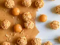 Piccoli bomboloni caramelle ricoperti di noccioline tritate, alcuni con un ripieno di caramello visibile.