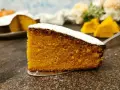 Una fetta di torta zucca senza glutine, soffice e dorata, cosparsa di zucchero a velo. Sullo sfondo, pezzi di zucca e un'altra torta.