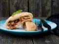 Delizioso strudel pere cioccolato e amaretti, con ripieno di mele e un tocco di menta, su un piatto blu cosparso di zucchero a velo.