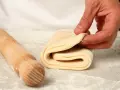 Mano che piega un impasto stratificato, pronto per diventare delizioso **ciasto francuskie**. Un mattarello è accanto.
