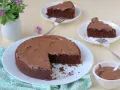 Deliziosa torta al cioccolato senza glutine con fecola di patate, ricoperta di glassa al cioccolato, servita su piatti bianchi con forchette.