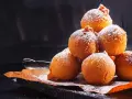 Pile di frittelle di mele e uvetta con lievito di birra, spolverate di zucchero a velo, su carta da forno.
