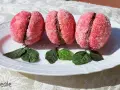 Tre dolci pesche abruzzesi ricoperte di zucchero, con un ripieno scuro, adagiate su un piatto bianco con foglie verdi.