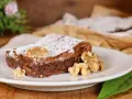 Una fetta di torta noci e cioccolato senza farina, cosparsa di zucchero a velo e decorata con noci intere.
