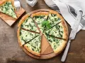 Torta salata spinaci e mozzarella, con un tocco di speck affumicato, tagliata a spicchi su un tagliere di legno.