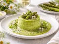 Delicato flan di asparagi con fonduta, guarnito con germogli freschi e fiori eduli. Un piatto primaverile che celebra il sapore degli asparagi.