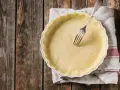 Pasta frolla salata con olio e parmigiano pronta per essere infornata. Una forchetta è appoggiata sulla base bucherellata.