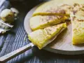 Focaccia di patate in padella con prosciutto cotto e formaggio, tagliata a spicchi su un tagliere di legno.
