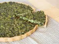 Una fetta di torta salata vegana spinaci, con una crosta dorata e un ripieno verde e cremoso, pronta per essere gustata.