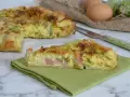 A slice of ham and zucchini quiche on a green napkin, with the rest of the quiche in the background.