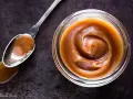 Un cucchiaio pieno di crema pasticcera al caramello salato, accanto a un barattolo dello stesso delizioso composto.