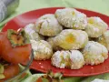 Biscotti ai cachi, dolcetti morbidi e profumati, cosparsi di zucchero a velo, accanto a cachi freschi.