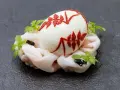Uovo sodo decorato con motivi rossi, adagiato su un letto di calamari crudi e guarnito con erbe aromatiche. Un barzotto uovo elegante.