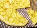 Schiacciata di patate con farina di ceci, guarnita con rosmarino fresco, su un tagliere di legno rustico.