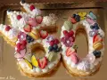 Una torta numero 60 decorata con panna, frutta fresca, macarons e farfalle. Una deliziosa ricetta torta numero per festeggiare.