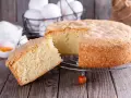 Un soffice ciasto drozdzowe, appena sfornato, con una fetta tagliata. Ingredienti per la torta lievitata sono visibili sullo sfondo.