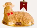 A decorative cake shaped like a lamb, with piped frosting and a red ribbon.