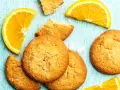 Biscotti all'arancia ricetta della nonna: dolci profumati e dorati, con spicchi d'arancia fresca su un tavolo di legno azzurro.