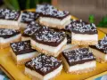 Deliziosi quadrotti cioccolato e cocco, stratificati con base croccante, crema bianca e copertura fondente, spolverati con cocco grattugiato.