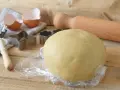 Impasto per kruche ciasto, stampini per biscotti, gusci d'uovo e mattarello pronti per preparare dolci deliziosi.