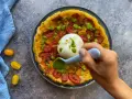 Tarte tatin pomodorini e burrata, con una mano che aggiunge un pesto verde.