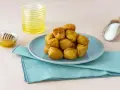 Un mucchio di turdiddri calabresi lucidi di miele su un piatto blu, con miele e farina a lato.