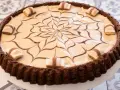 Torta con base croccante al cacao, ripiena di crema chiara e decorata con cioccolato fondente e pezzi di Kinder Bueno White.