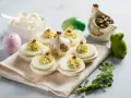 Uova ripiene vegetariane con ceci, guarnite con capperi e erbe aromatiche, su un piatto decorato con galline e uova pasquali.