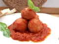 Polpette di pane in umido, un piatto confortante con pomodoro e basilico, accompagnato da fette di pane.