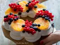 Delizioso tort pavlova a forma di corona, decorato con fette d'arancia, ribes rosso e mirtilli.