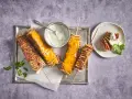 Tortilla kebab su spiedini, alcuni ricoperti di formaggio fuso, serviti con salsa allo yogurt e prezzemolo.