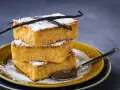 Tre fette impilate di torta di riso fiorentina, spolverate di zucchero a velo e decorate con baccelli di vaniglia.