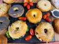 Varietà di bagel dolci e salati, alcuni con semi di sesamo, altri con semi di papavero, accompagnati da pomodorini e salmone affumicato.