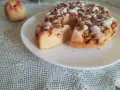 Delizioso ciasto z brzoskwiniami, cosparso di zucchero a velo, su un piatto bianco, accanto a una pesca fresca.
