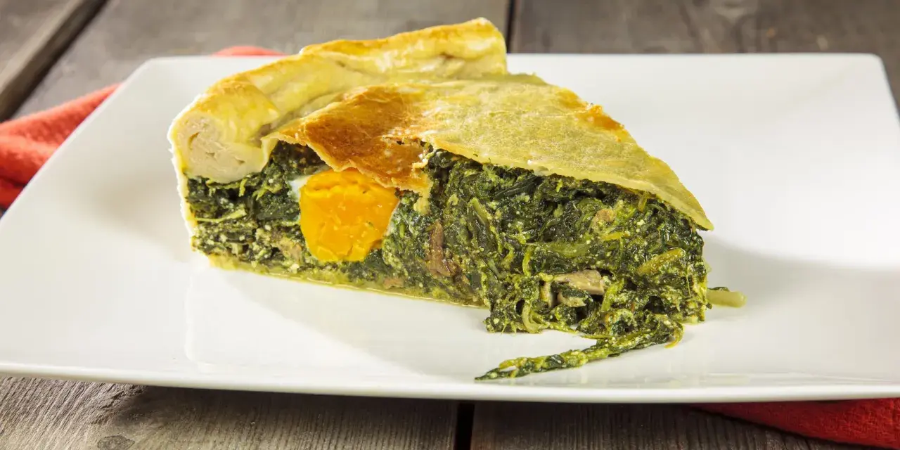 Una fetta di torta di bietole e ricotta senza sfoglia, con un uovo intero al centro, su un piatto bianco.