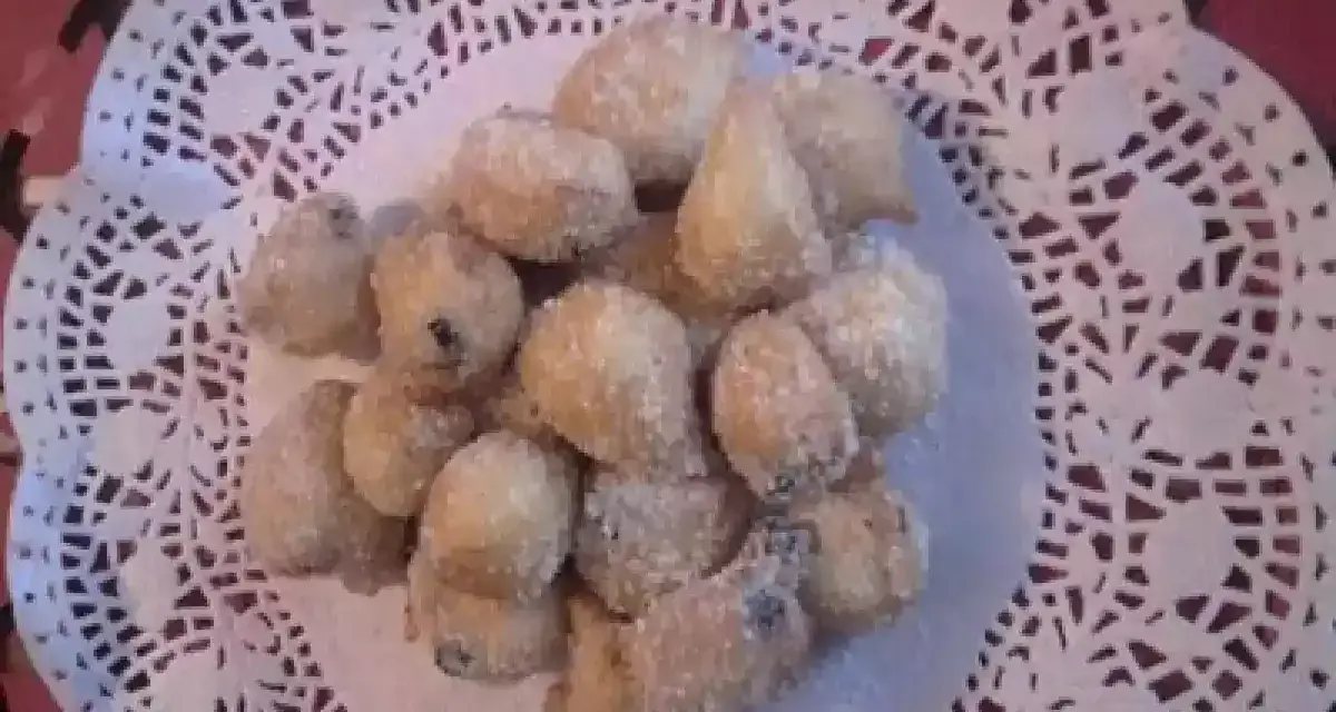 Un mucchietto di castagnole montersino, dolcetti dorati e zuccherati, adagiati su un centrino di pizzo bianco.
