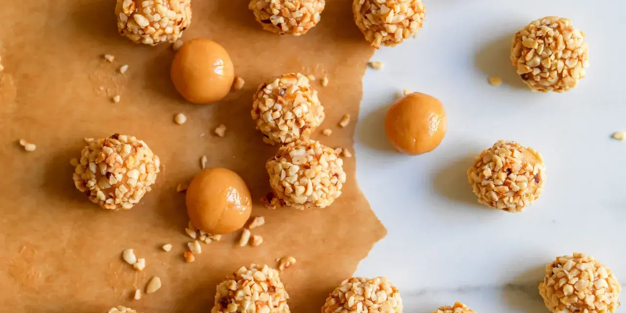 Piccoli bomboloni caramelle ricoperti di noccioline tritate, alcuni con un ripieno di caramello visibile.
