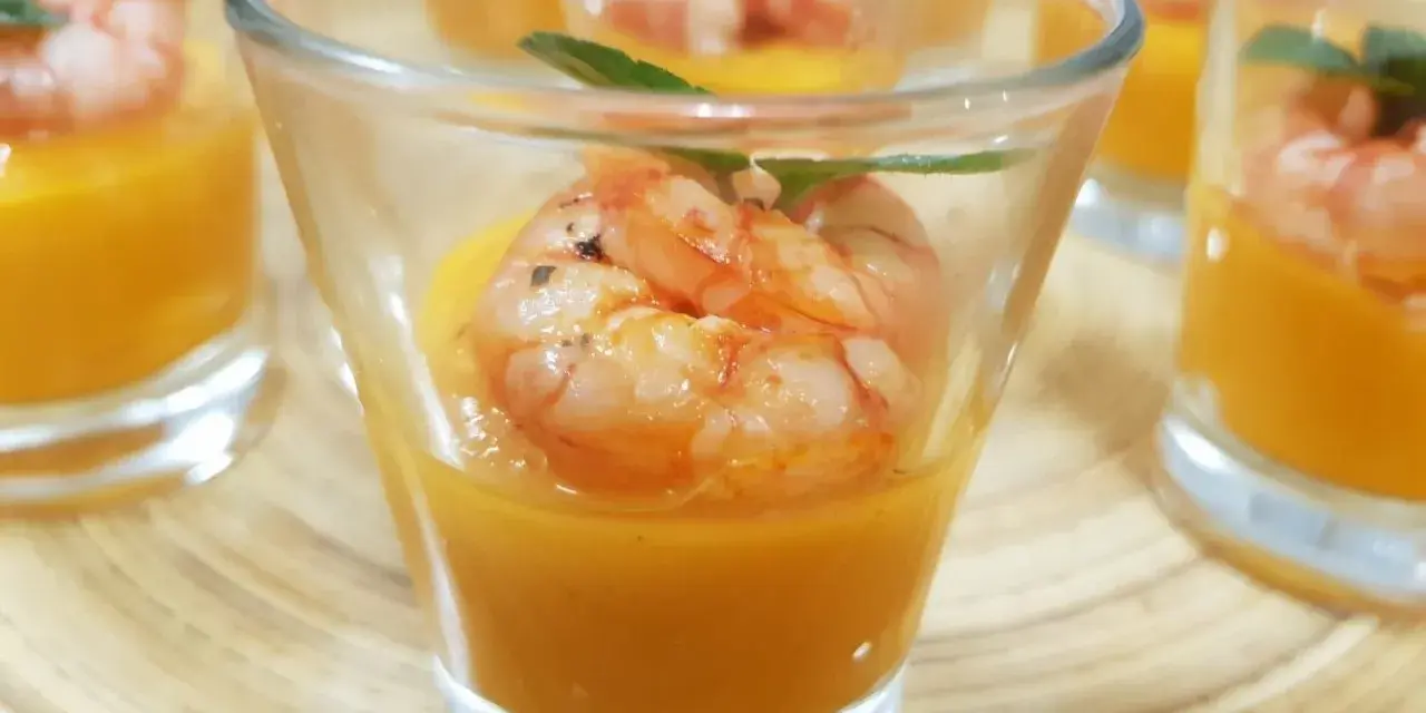 Deliziosi gamberi aperitivo in bicchierini con crema arancione e foglioline verdi.