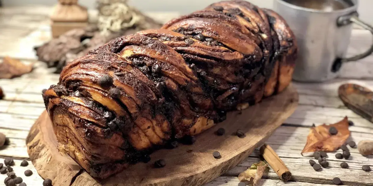 Babka ponczowa, intrecciata e ricca di gocce di cioccolato, pronta per essere gustata con una tazza di caffè.