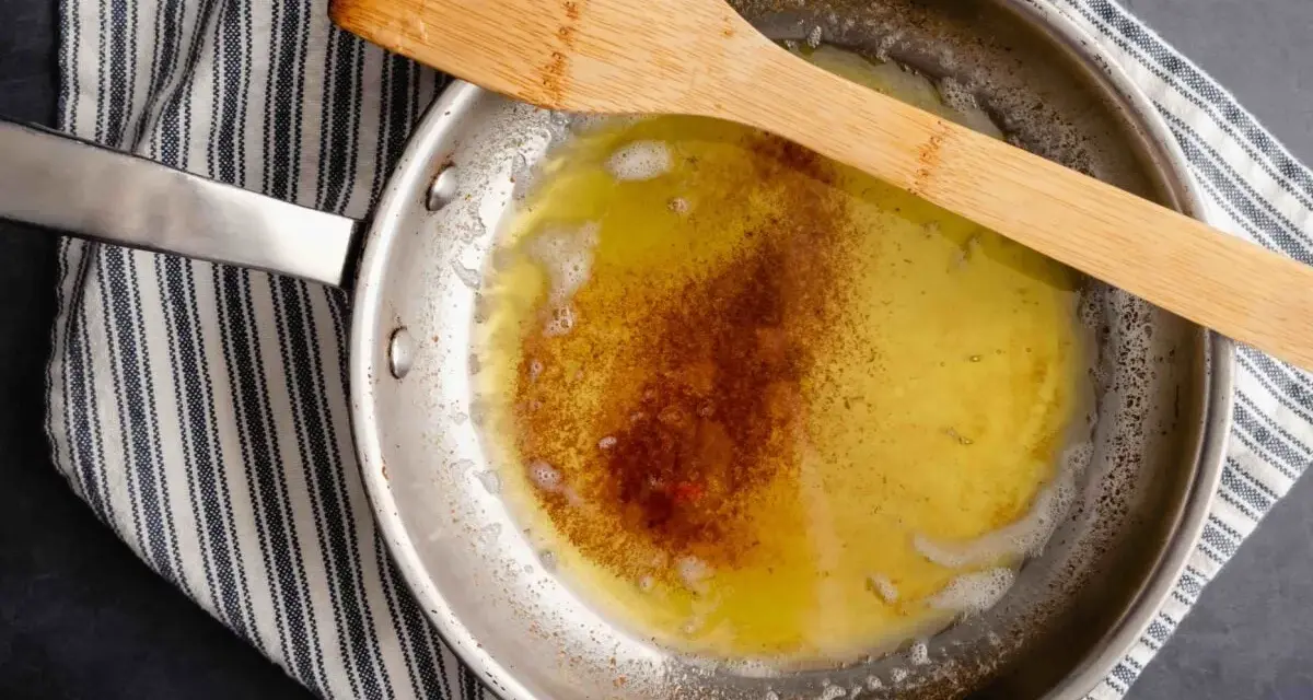 Burro alla nocciola che si scioglie in padella, con una spatola di legno appoggiata sopra.
