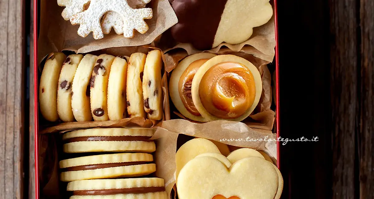 Scatola piena di deliziosi ciasteczka maślane: a fiocco di neve, al cioccolato, con ripieno di caramello e a forma di cuore.