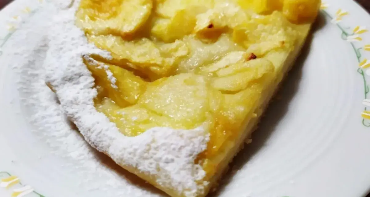 Una fetta di pizza con le mele, cosparsa di zucchero a velo, su un piatto bianco con decorazioni floreali.