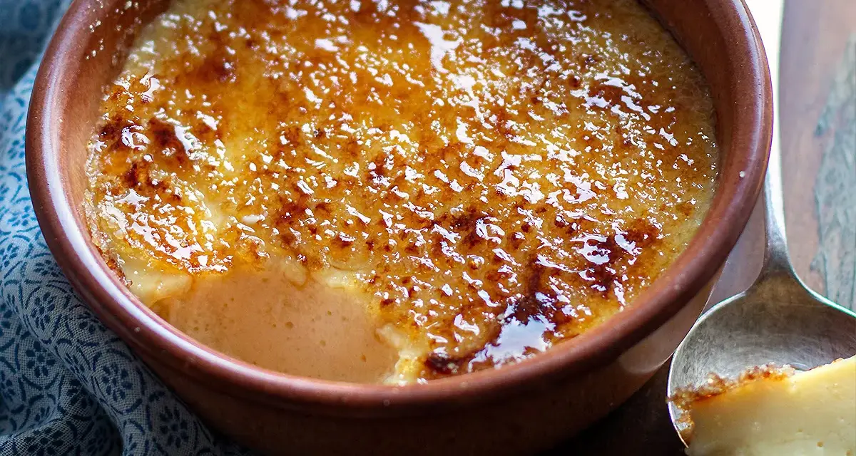 Un delizioso krem kataloński con crosta caramellata dorata, servito in una ciotola di terracotta.