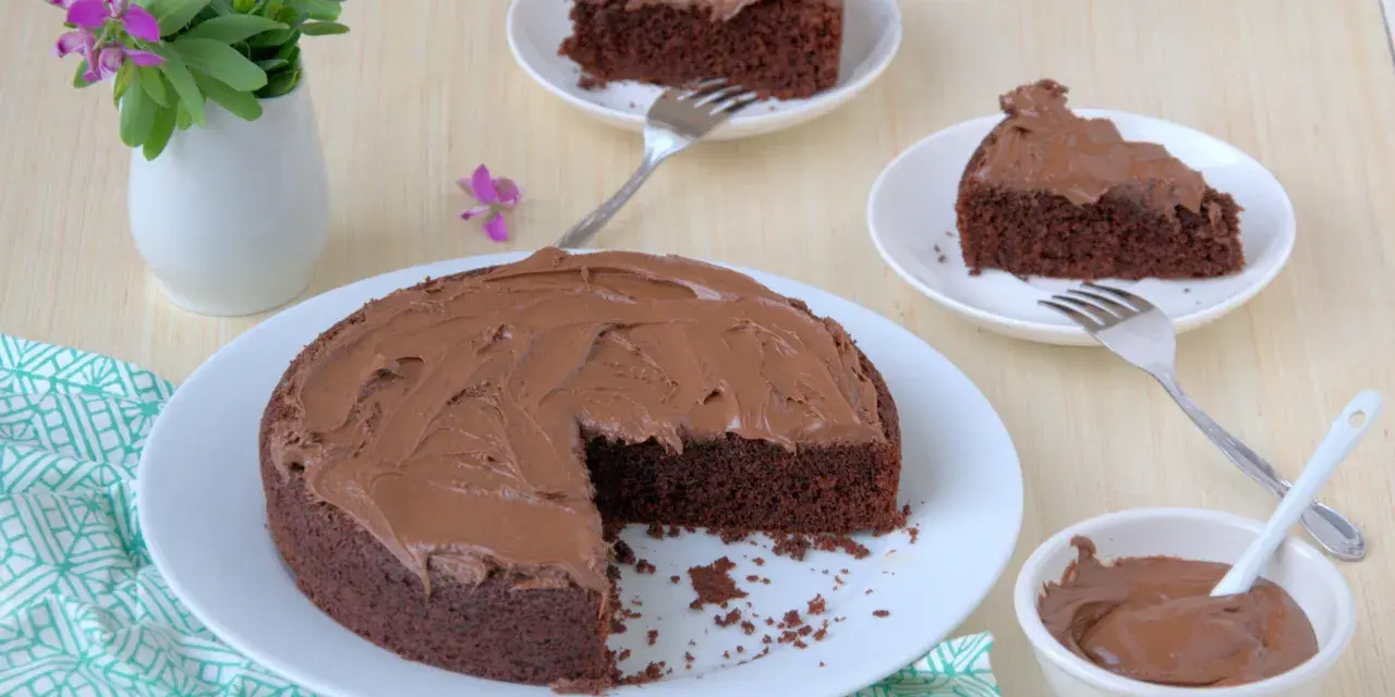 Deliziosa torta al cioccolato senza glutine con fecola di patate, ricoperta di glassa al cioccolato, servita su piatti bianchi con forchette.