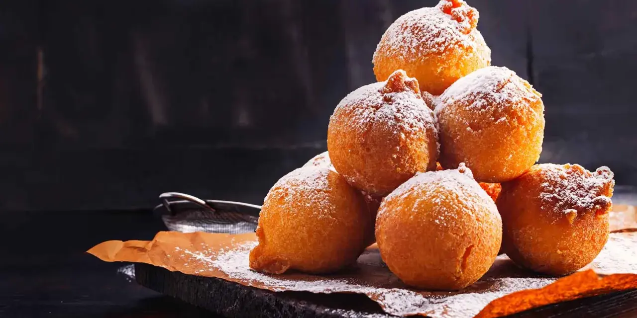 Pile di frittelle di mele e uvetta con lievito di birra, spolverate di zucchero a velo, su carta da forno.