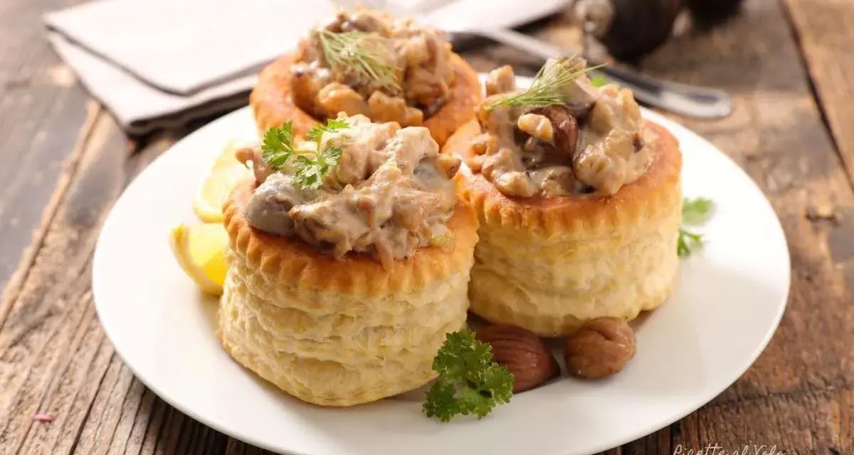 Tre vol-au-vent con funghi cremosi, guarniti con prezzemolo e aneto, su un piatto bianco con spicchi di limone.