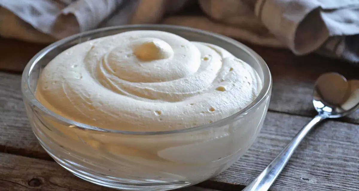 Una ciotola di soffice crema al mascarpone senza lattosio, pronta per essere gustata. Un cucchiaino argentato attende accanto.