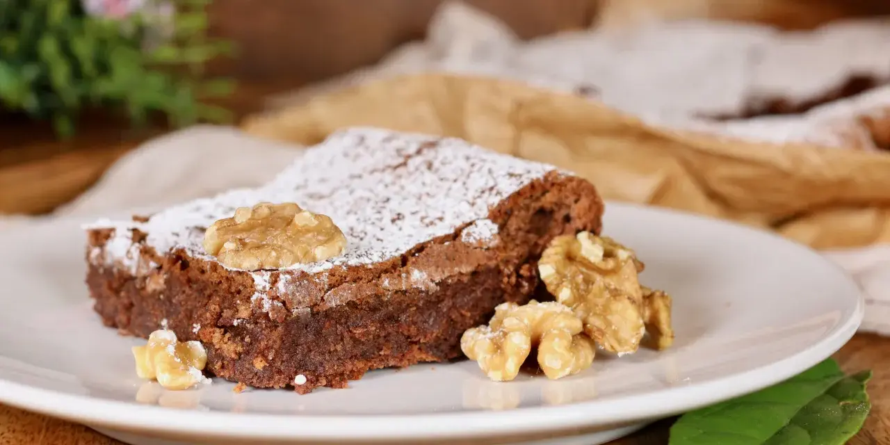 Una fetta di torta noci e cioccolato senza farina, cosparsa di zucchero a velo e decorata con noci intere.