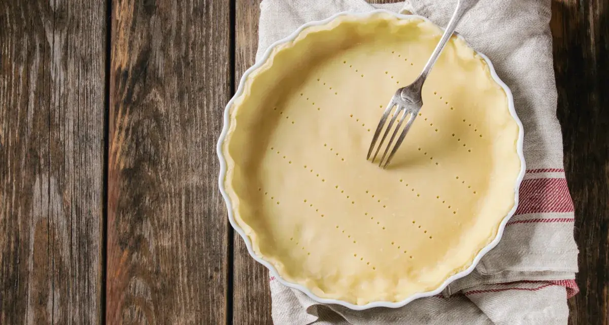Pasta frolla salata con olio e parmigiano pronta per essere infornata. Una forchetta è appoggiata sulla base bucherellata.